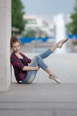 Girl ballerina in jeans, a plaid shirt and pointe shoes dancing in the city on the street © Tatiana