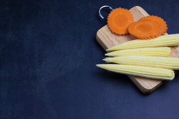 Baby corn and carrots on the chopping board. Copy area