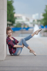 Girl ballerina in jeans, a plaid shirt and pointe shoes dancing in the city on the street © Tatiana