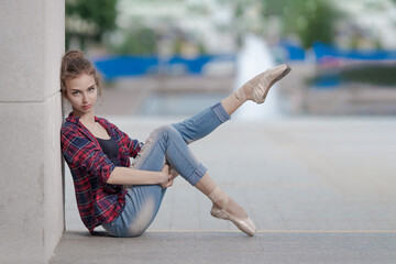 Girl ballerina in jeans, a plaid shirt and pointe shoes dancing in the city on the street © Tatiana