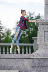 Girl ballerina in jeans, a plaid shirt and pointe shoes dancing in the city on the street © Tatiana