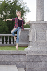 Girl ballerina in jeans, a plaid shirt and pointe shoes dancing in the city on the street © Tatiana