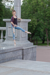 Girl ballerina in jeans, a plaid shirt and pointe shoes dancing in the city on the street © Tatiana