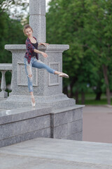 Girl ballerina in jeans, a plaid shirt and pointe shoes dancing in the city on the street © Tatiana