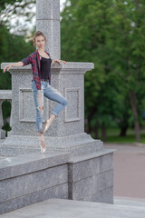 Girl ballerina in jeans, a plaid shirt and pointe shoes dancing in the city on the street © Tatiana