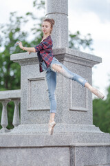 Girl ballerina in jeans, a plaid shirt and pointe shoes dancing in the city on the street © Tatiana
