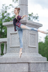 Girl ballerina in jeans, a plaid shirt and pointe shoes dancing in the city on the street © Tatiana