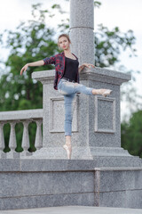 Girl ballerina in jeans, a plaid shirt and pointe shoes dancing in the city on the street © Tatiana