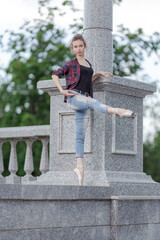 Girl ballerina in jeans, a plaid shirt and pointe shoes dancing in the city on the street © Tatiana