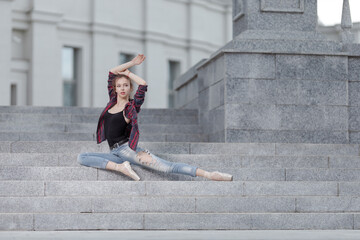 Girl ballerina in jeans, a plaid shirt and pointe shoes dancing in the city on the street © Tatiana