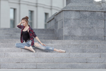 Girl ballerina in jeans, a plaid shirt and pointe shoes dancing in the city on the street © Tatiana