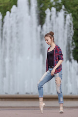 Girl ballerina in jeans, a plaid shirt and pointe shoes dancing in the city on the street © Tatiana