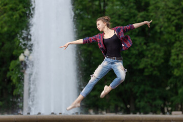 Girl ballerina in jeans, a plaid shirt and pointe shoes dancing in the city on the street © Tatiana