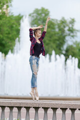 Girl ballerina in jeans, a plaid shirt and pointe shoes dancing in the city on the street © Tatiana