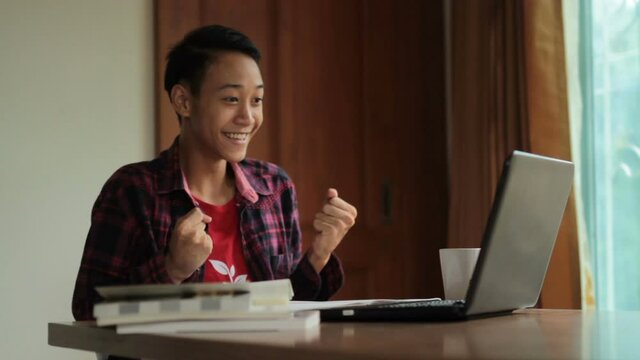 Teen of asian man pass an exam and feeling excited at front of laptop computer while living at home.