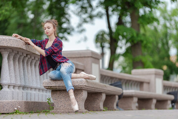 Girl ballerina in jeans, a plaid shirt and pointe shoes dancing in the city on the street © Tatiana