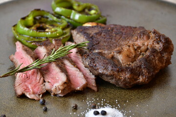 Close up Sliced medium rare grilled steak with salt,Bell pepper and rosemary placed on plate.