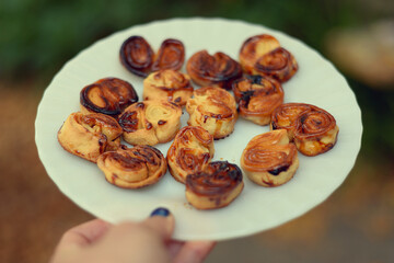 Homemade sweet puff pastry cookies on plate, in woman's hand