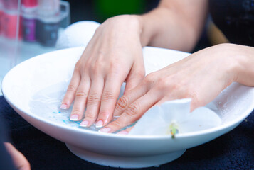 female hands in a bowl with water to soften nails