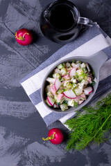 Okroshka soup with radish, sausage, cucumber, egg and potato in a ceramic bowl. Kvass in glass jug on the grey table. Russian cuisine meal