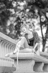 Black and white photo of a ballerina girl in jeans and pointe shoes, dancing and posing in the city on the street © Tatiana