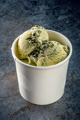 Pistachio ice cream balls with nuts in a paper white glass on a gray stone background