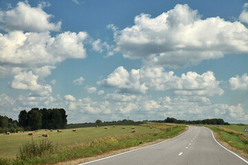 Long road. Highway among white clouds in a blue sky. summer landscape green trees and grass