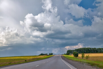 Fototapeta na wymiar Long road. Highway among white clouds in a blue sky. summer landscape green trees and grass