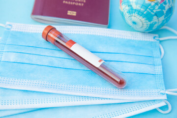 a top view of a coronavirus blood test tube with coronavirus write it on, above some masks, near a red passport and world 