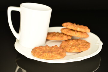 Fragrant tasty, sweet grain cookies with a ceramic cup and saucer, close-up, on a black background.