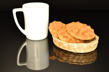 Fragrant tasty, sweet cereal cookies in a straw basket and a white ceramic cup, close-up, on a black background.