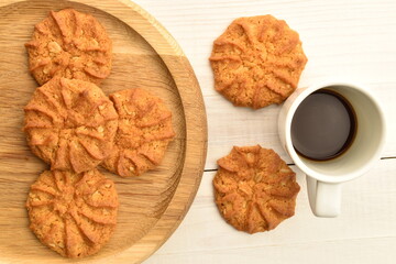 Fragrant tasty, sweet cereal cookies on a round wooden tray with a white cup, close-up, on a wooden table.