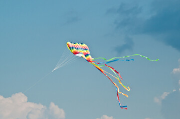 Front, bottom view, far distance of a colorful child's kite, flying in a stiff breeze at a tropical...