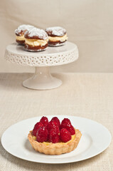 Top, front view, medium distance of a white plate with freshly picked strawberries and a ceramic, pedestal, display plate, with freshly baked, pasty, filled with whipped cream