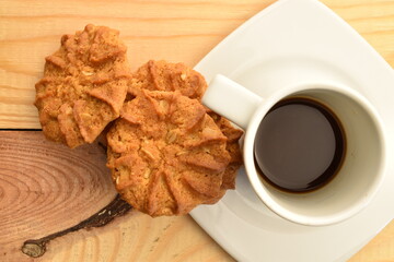 Fragrant tasty, sweet cereal cookies with a white ceramic saucer and a cup, close-up, on a wooden table.