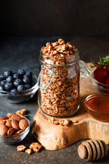 Homemade oatmeal granola in open glass jar on dark background.