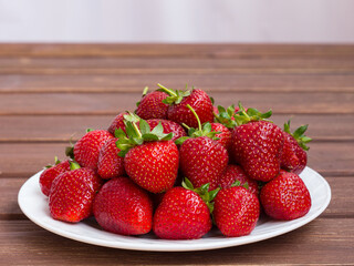 ripe red strawberries on a white plate on a wooden table