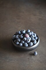 Blueberries in a black ceramic bowl. Dark concrete background