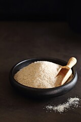 Psyllium hask in a black ceramic bowl. Dark concrete background