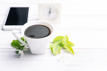 Workspace composition with coffee cup ,mobile phone,alarm clock and flowers on white wood table