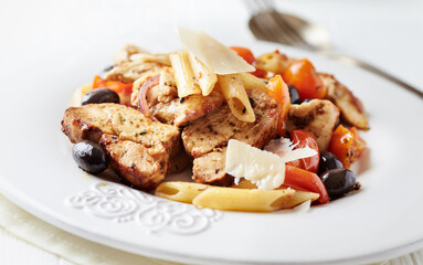 Penne pasta with pork tenderloin, cherry tomatoes, black olives and hard cheese. Close up. 