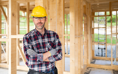 Proud worker posing on building site with frame house construction in background