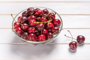 Bowl with red cherries on white wooden background. Fresh sweet cherry berry