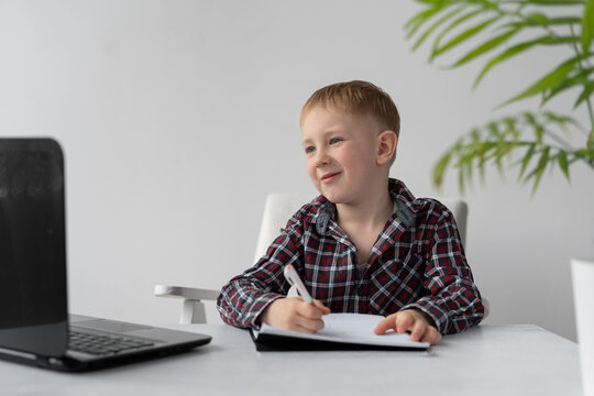 A schoolboy is doing quarantine homework at home. Distance learning and lessons. The boy sits on a chair at the table. The task in the laptop. Online education and quarantine.