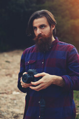 Young bearded man taking photo with his digital camera, handsome hipster tourist checking out the sights in nature landscape, hiker looking out across the nature holding his professional camera, flare