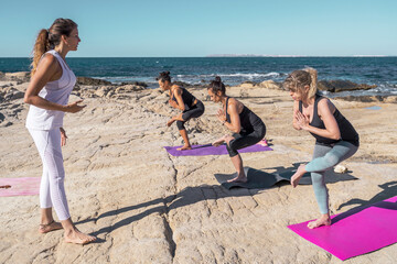Fototapeta premium Group of people in a yoga class on the beach on sunny day. The group of people is made up of men and women of different ages dressed in sports clothes.