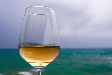 A glass of white wine against the blue sea, close-up