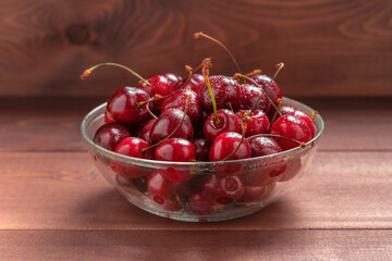Bowl filled with ripe red cherries. Brown wooden background. Cherry berry on table, rustic composition