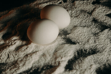 Two eggs lie in flour on a black background