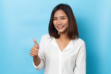 Happy asian young woman smiling against made finger thumbs up OK gesture on blue background